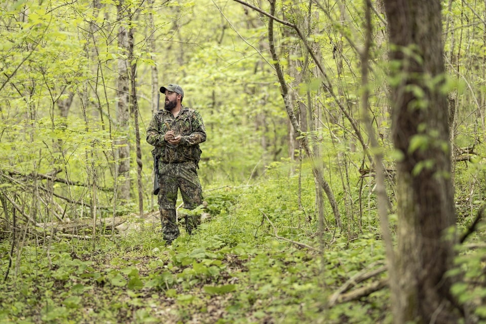 Man in camo using a turkey call in green wooded land