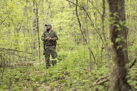 Man in camo using a turkey call in green wooded land