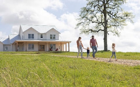 Family of four walking down the driveway with their rural family home in the background.