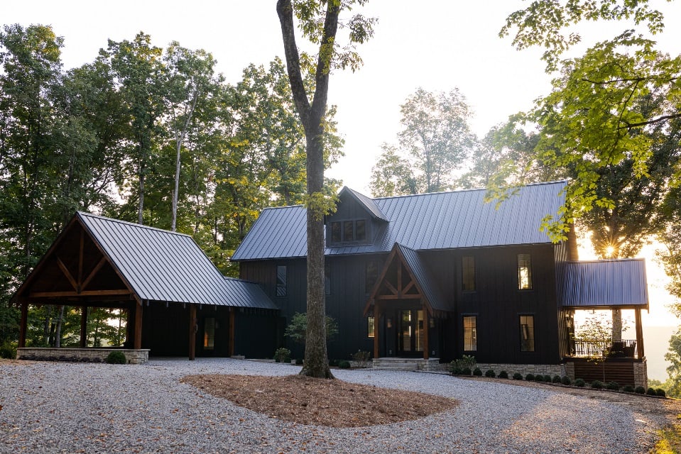 Black clad home with black metal roof in a wooded area with the sunrise in the background