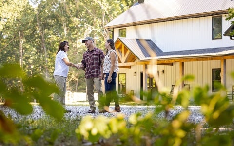 A couple shaking hands with a Rural 1st loan officer in front of their newly constructed rural home.