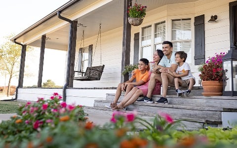 A family sitting on the front porch steps of their new rural home
