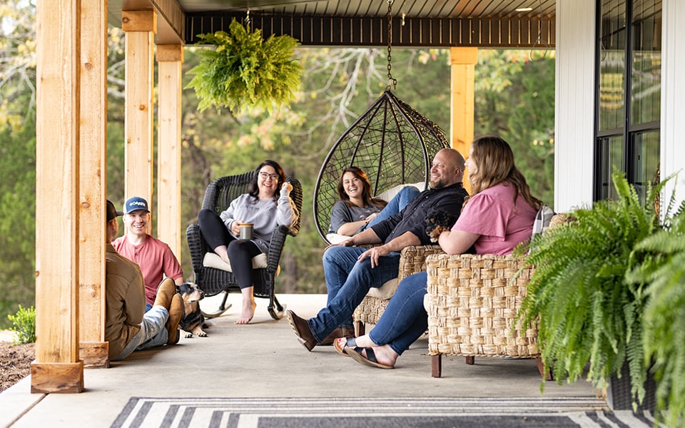 A family of six and their dog, laughing together on the porch of their newly built rural home.