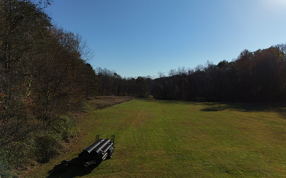 Grassy and wooded area on a plot of rural land with a trailer in the foreground.