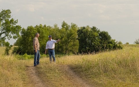 Two people standing on a rural plot of bare land bought with land loans from Rural 1st.