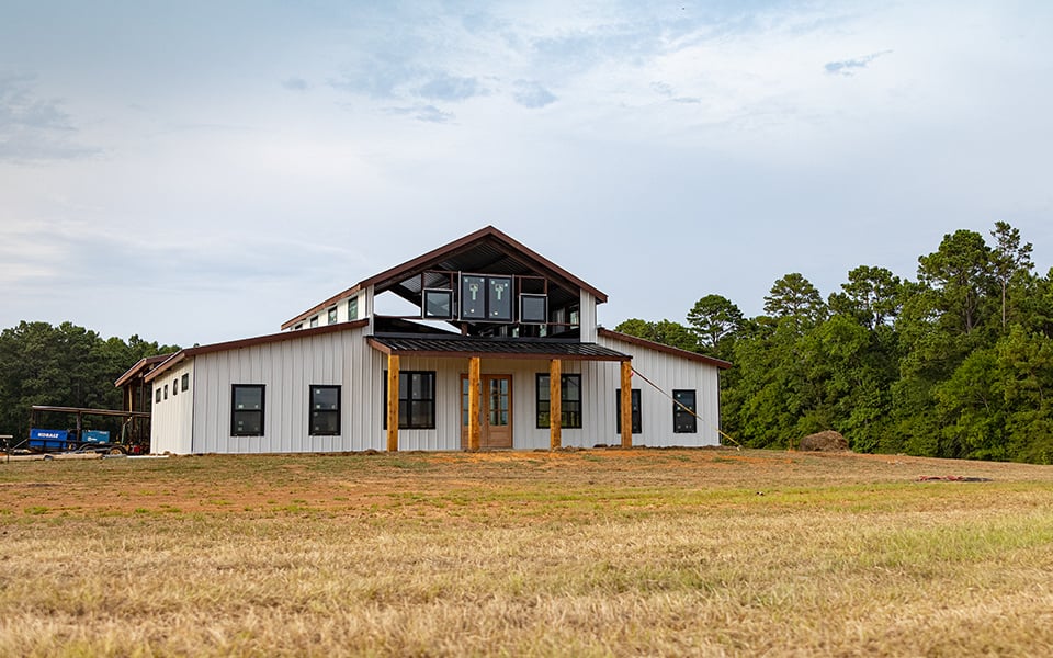 An under-construction barndominium with open land in front of it.