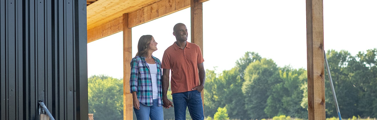 A couple standing on the porch of their under-construction rural home.