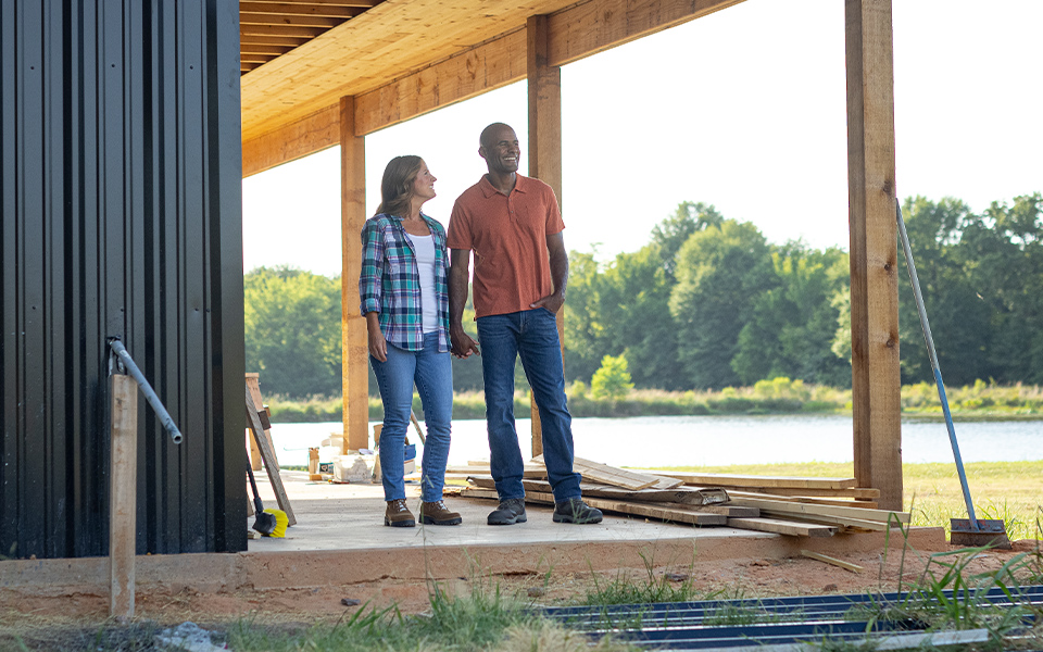 A couple standing on the porch of their under-construction rural home.