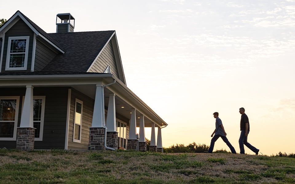 Two people walking at sunset through the yard to their new rural home.