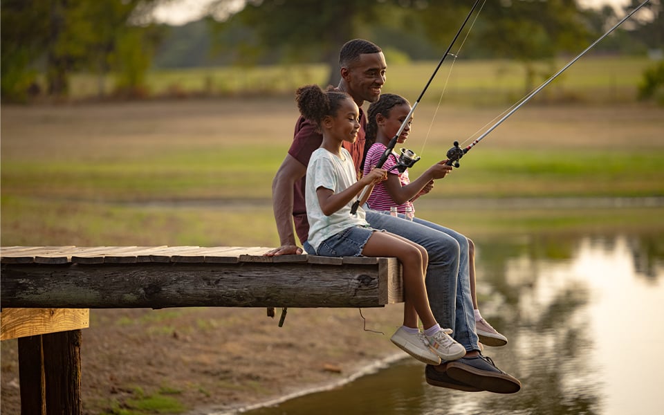 A father and his two daughters sitting on a dock and fishing after getting financing for land loans from Rural 1st.