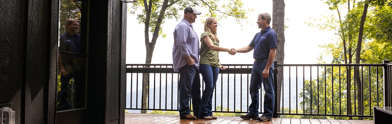 A couple shaking hands with a Rural 1st loan officer on the porch of their new rural home.