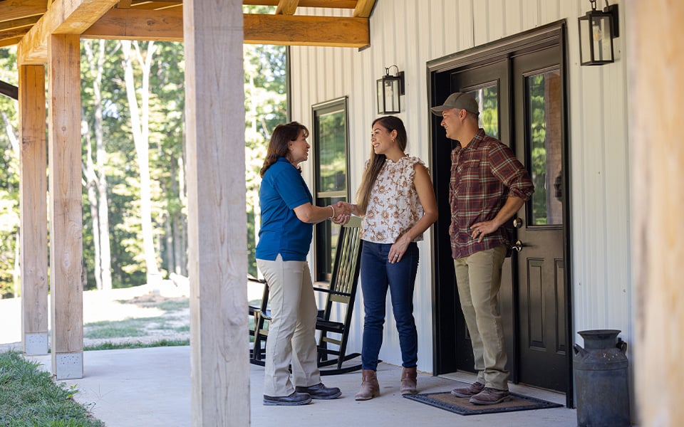 A couple having a conversation with a Rural 1st loan officer on the porch of their new rural home.