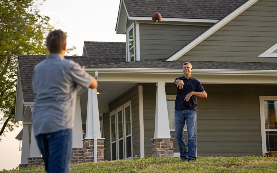 A father and son throwing a football in the yard after building a home on land.